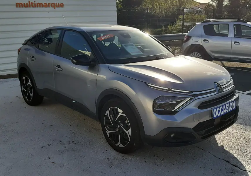 Vue 3/4 avant d'une Citroën C4 gris métallisé 2023 avec jantes bicolores et plaque "OCCASION" visible.