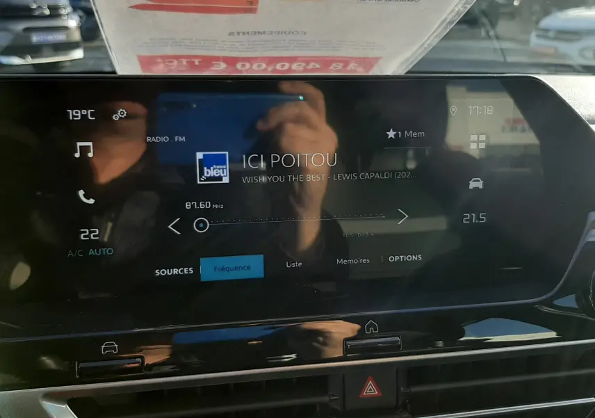 Vue intérieure du tableau de bord de la Citroën C4 2023, écran tactile affichant la radio FM et commandes climatisation.