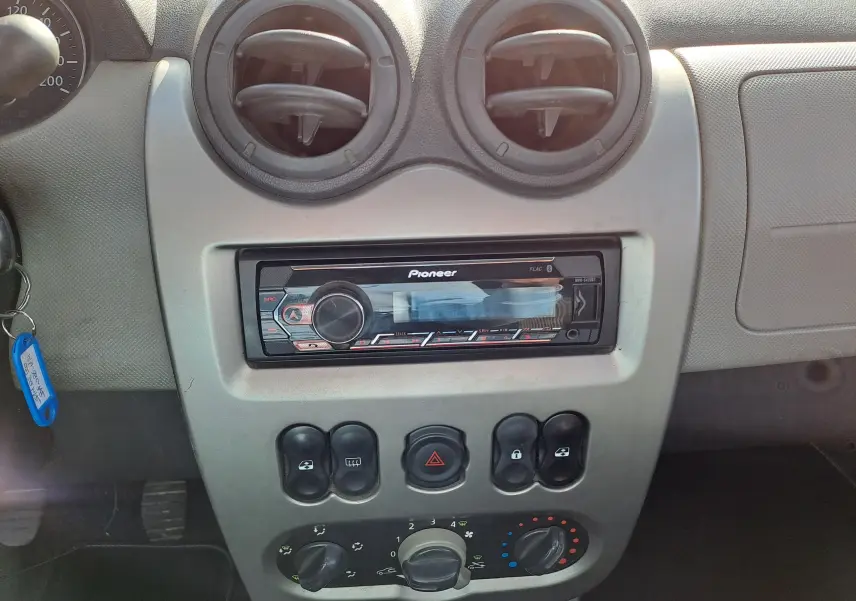 Vue rapprochée du tableau de bord gris clair de la Dacia Sandero 2010 avec autoradio Pioneer et commandes de climatisation.