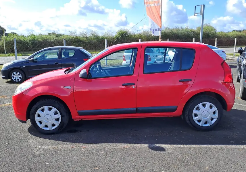 Vue latérale gauche d'une Dacia Sandero rouge de 2010, compacte avec jantes en acier et poignées noires.