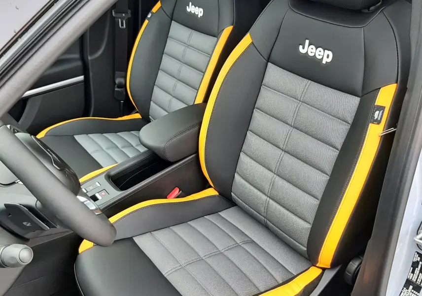 Vue intérieure côté conducteur du Jeep Avenger 2025, sièges gris et noir avec surpiqûres jaunes et logo Jeep blanc.