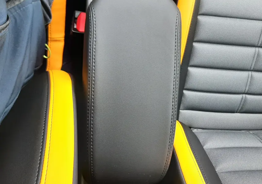 Gros plan sur l'accoudoir central noir avec surpiqûres, entouré de sièges gris et inserts jaunes dans l'habitacle Jeep Avenger.