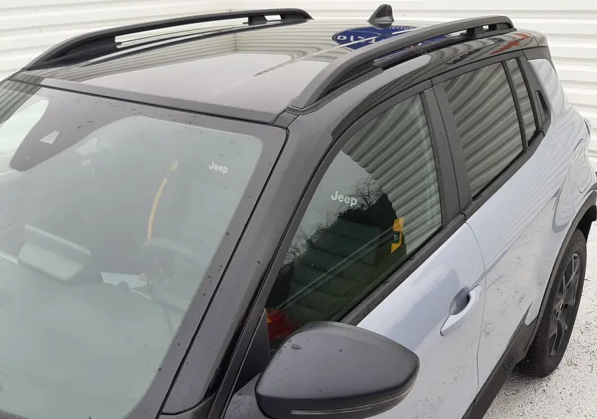 Vue 3/4 avant droit du Jeep Avenger gris Storm avec toit noir et barres de toit noires visibles.