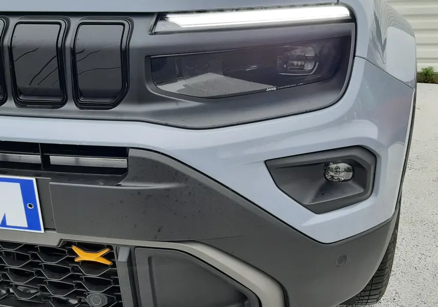 Gros plan sur l'avant droit du Jeep Avenger 2025 en Storm Grey, avec phare LED et calandre noire distinctive.