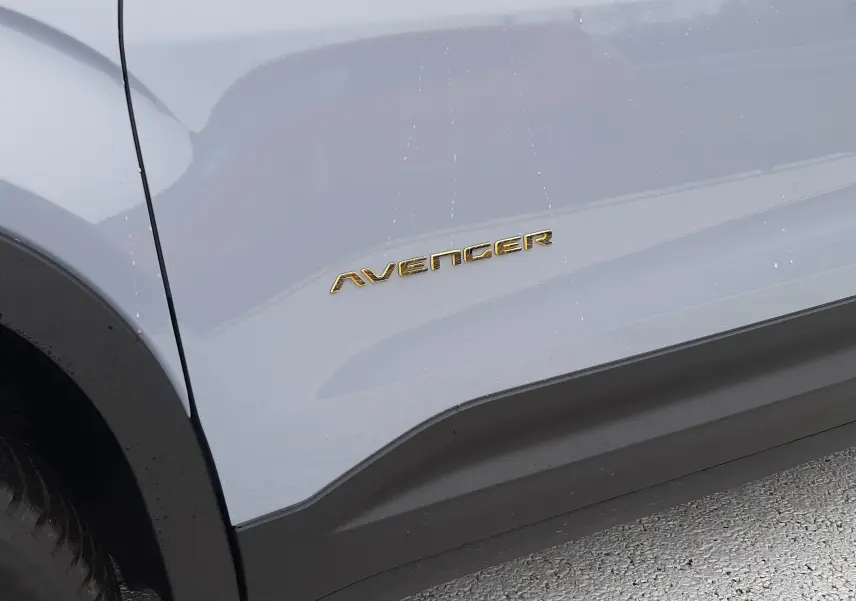 Gros plan sur le côté gauche gris Storm du Jeep Avenger avec le logo doré Avenger visible sur la portière.