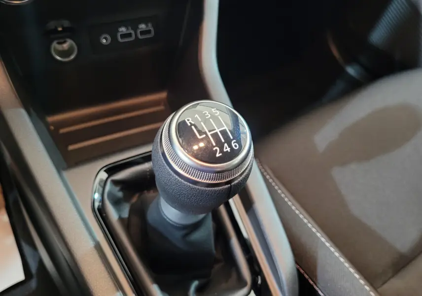 Gros plan sur le levier de vitesses manuel noir de la Renault Clio gris foncé, avec ports USB et prise 12V en arrière-plan.