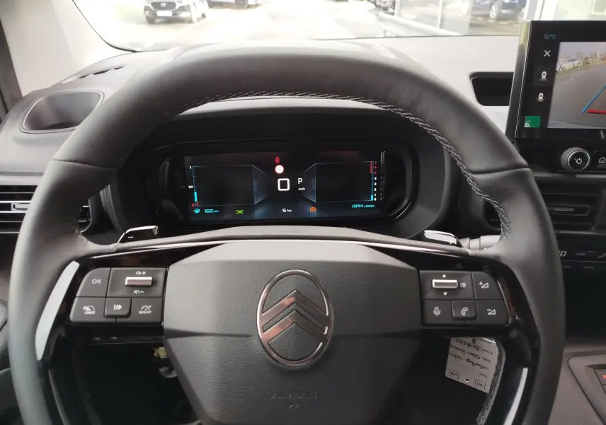 Vue intérieure centrée sur le volant noir du Citroën Berlingo 2025 avec tableau de bord numérique et écran de caméra de recul.