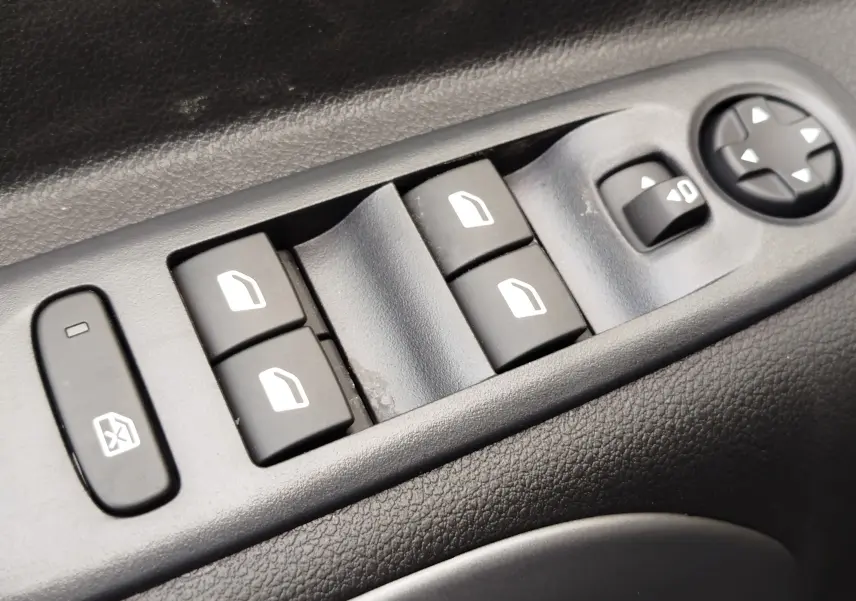Détail des commandes de lève-vitres et réglage des rétroviseurs sur la porte côté gauche d’un Citroën Berlingo bleu Kiarma.
