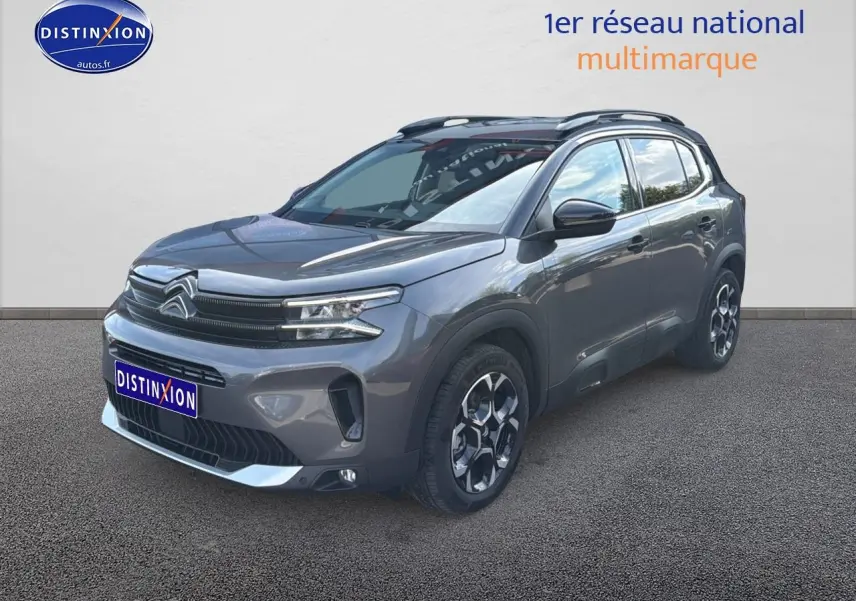 Vue 3/4 avant droit d'un Citroën C5 Aircross gris platinium avec barres de toit et jantes alu distinctives.