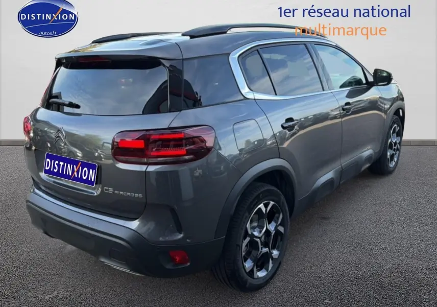 Vue 3/4 arrière droite d'un Citroën C5 Aircross gris platinium avec barres de toit et jantes alu distinctives.