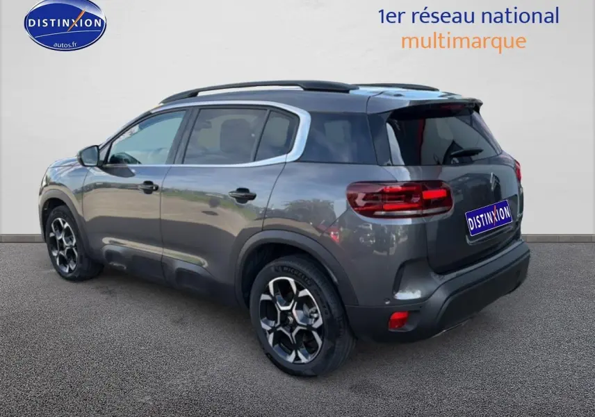 Vue 3/4 arrière droit d'un Citroën C5 Aircross gris platinium avec barres de toit et jantes alu noires.