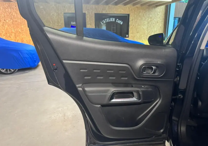 Vue intérieure rapprochée des sièges avant gris foncé du Citroën C5 Aircross 2022 avec accoudoir central et porte-gobelets.