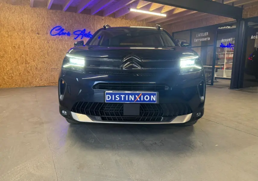 Vue de face du Citroën C5 Aircross bleu avec phares LED allumés et barres de toit visibles en intérieur showroom.