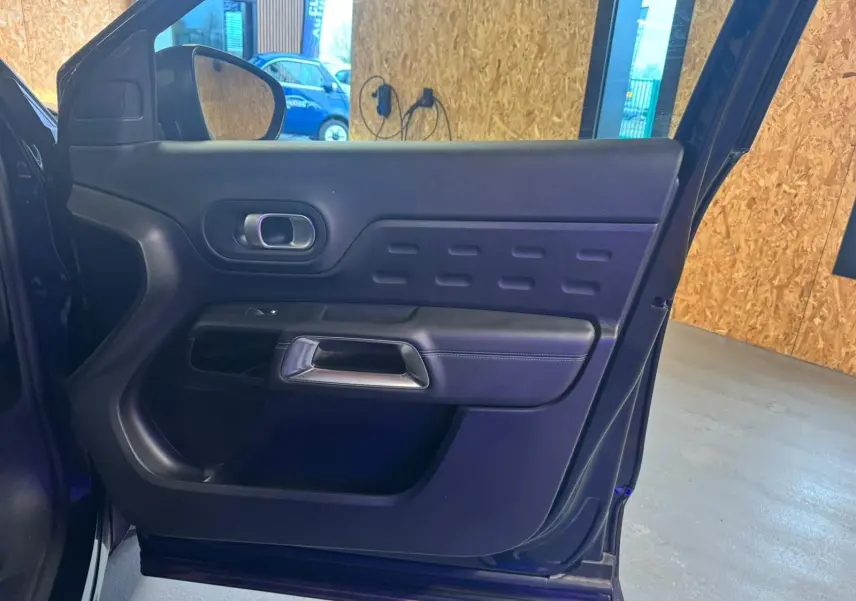 Vue intérieure côté gauche de la porte avant d’un Citroën C5 Aircross bleu avec poignée argentée et panneau noir texturé.
