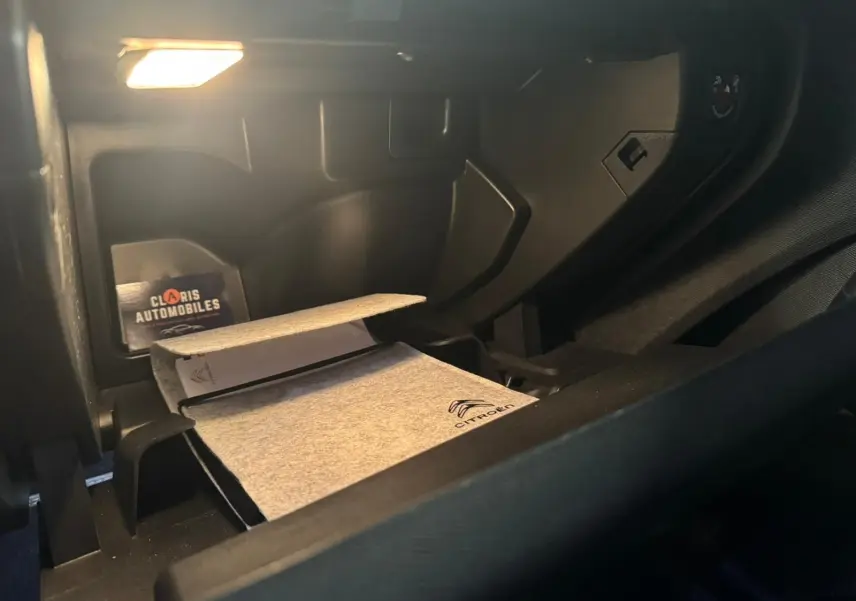 Vue intérieure du coffre à gants ouvert du Citroën C5 Aircross bleu avec manuel et éclairage intérieur allumé.