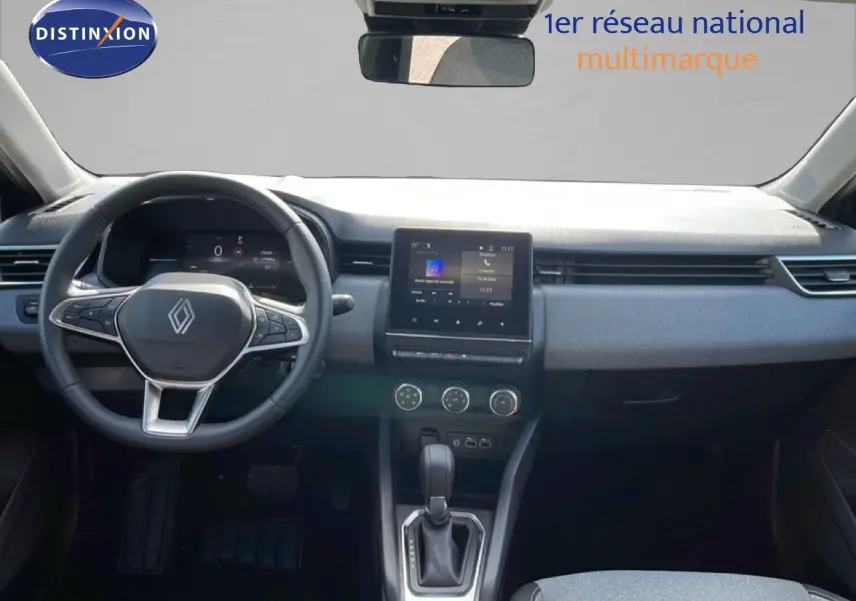Vue intérieure avant de la Renault Clio 2025, tableau de bord gris avec écran tactile central et volant multifonction.