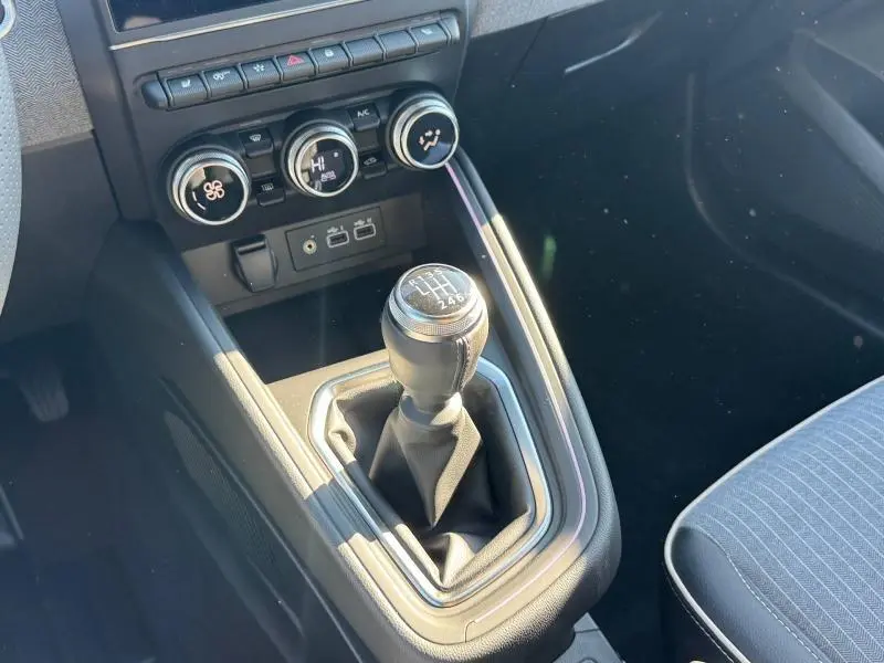 Vue rapprochée de la console centrale de la Renault Clio orange 2025, avec levier de vitesse manuel et commandes de climatisation.