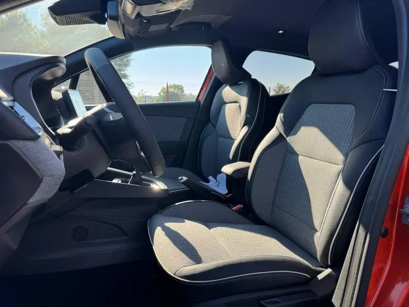 Vue intérieure côté conducteur de la Renault Clio orange 2025, sièges TEP noir avec inserts brun et volant cuir multifonction.