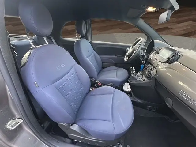 Vue intérieure côté conducteur de la Fiat 500 gris foncé 2022 avec sièges bleu marine et tableau de bord brillant.