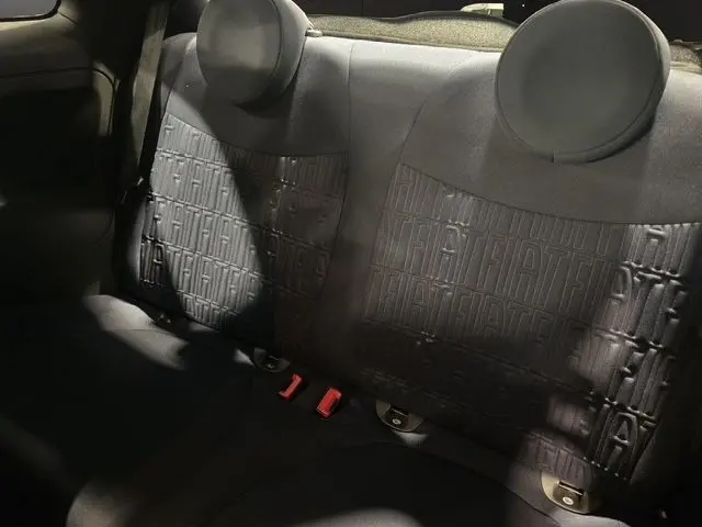 Vue rapprochée de la banquette arrière noire avec motifs FIAT embossés du Fiat 500 gris foncé, éclairage tamisé.