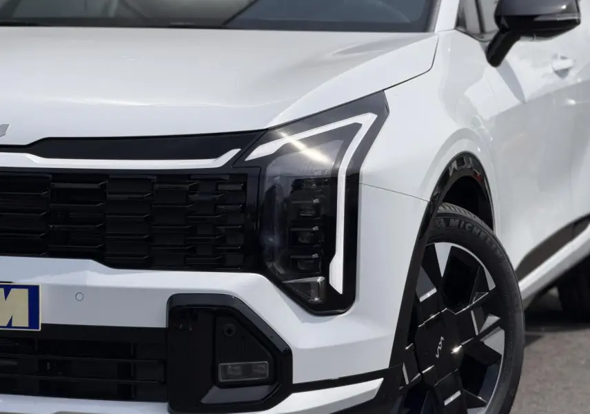 Gros plan sur l'avant droit du KIA Sportage blanc 2026, mettant en valeur le phare LED et la jante alliage noire.