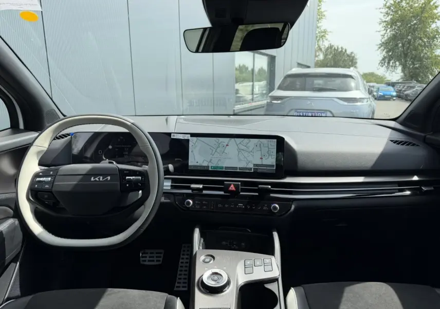 Vue intérieure avant du Kia Sportage 2026, tableau de bord noir avec écran tactile large et volant bi-ton clair et noir.