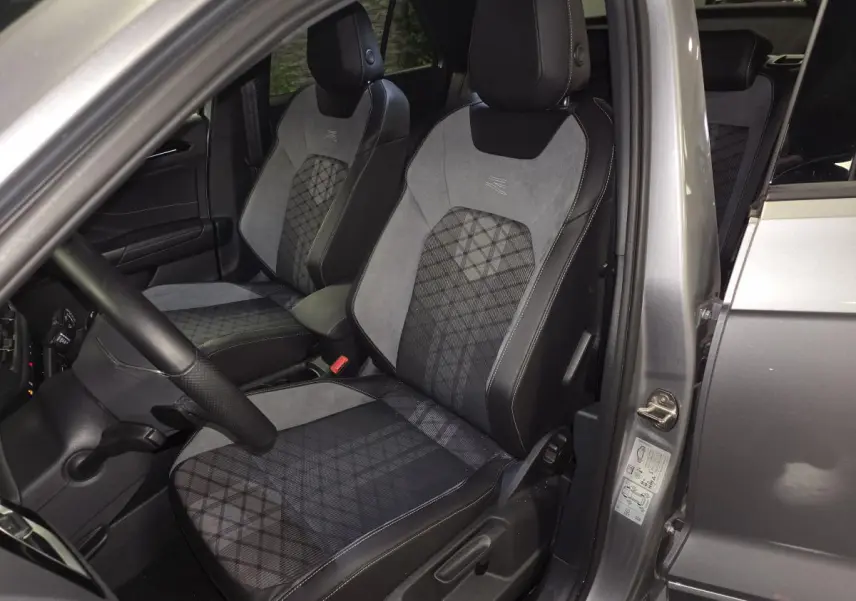 Vue intérieure côté conducteur du Volkswagen T-Roc gris 2025, mettant en valeur les sièges avant R-Line en tissu et similicuir.