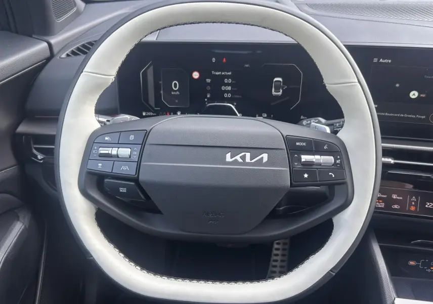 Vue rapprochée du volant bi-ton clair et noir du KIA SPORTAGE 2026 avec tableau de bord digital en arrière-plan.