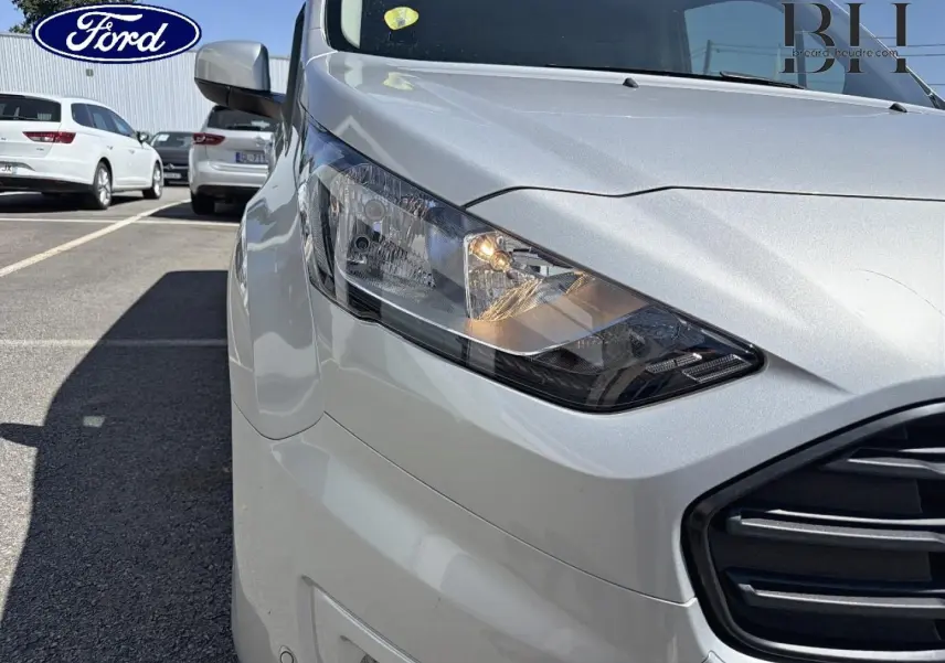 Gros plan sur l'avant droit du Ford Transit Connect gris lunaire métallisé, mettant en valeur le phare et la calandre.