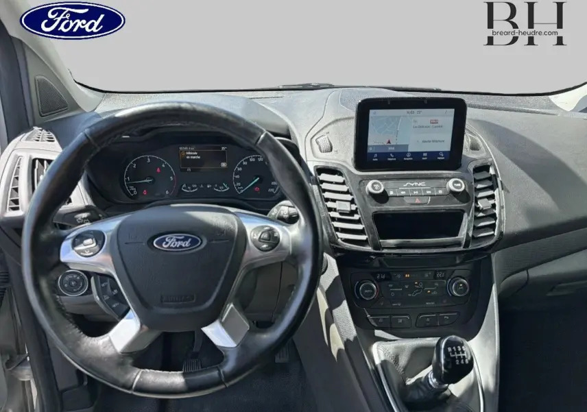 Vue intérieure centrée sur le volant et la console centrale du Ford Transit Connect gris lunaire avec écran tactile et levier manuel.