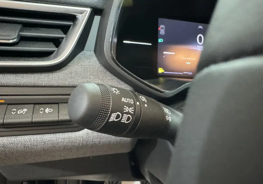 Gros plan sur la commande des phares et tableau de bord numérique de la Renault Clio gris clair, vue côté conducteur.