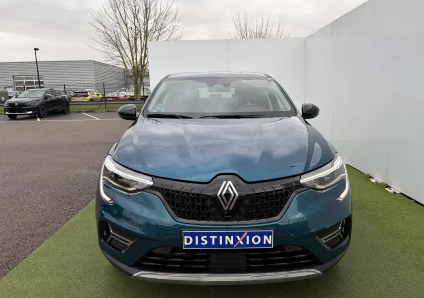 Vue avant d'une Renault Arkana bleu Zanzibar métallisé avec calandre noire et phares LED allumés sur fond extérieur neutre.