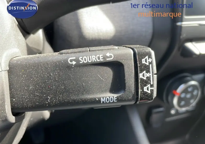 Gros plan sur la commande au volant Renault Clio 2025, bouton source et mode en plastique noir texturé.