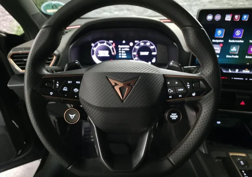 Vue rapprochée du volant noir perforé de la CUPRA Formentor avec logo cuivré et tableau de bord digital allumé.