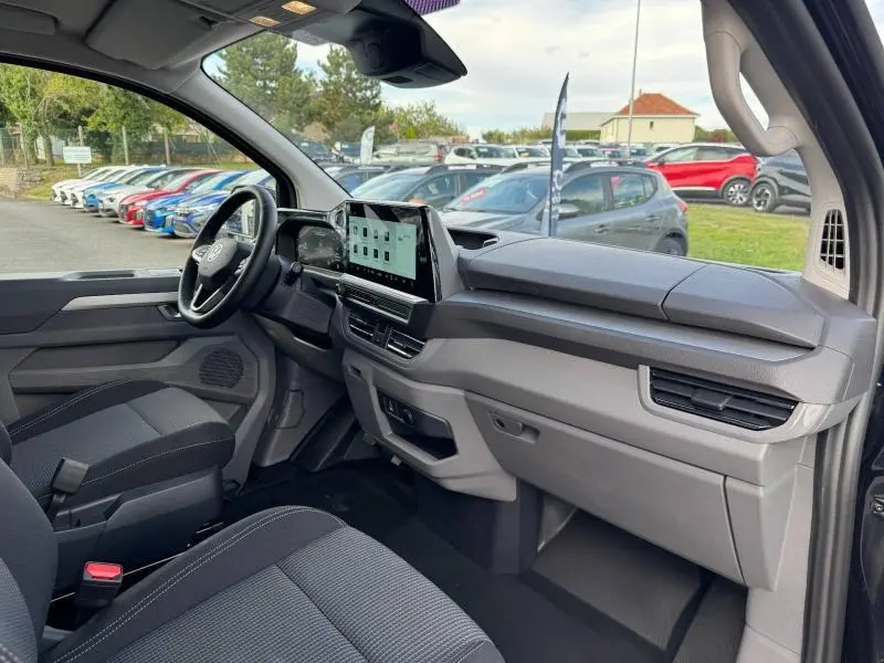 Vue intérieure côté passager du Volkswagen Transporter Procab 2025, tableau de bord moderne avec écran tactile et sièges tissu gris.