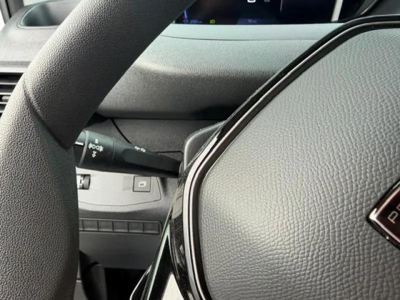Gros plan sur le volant noir texturé et la commande des feux à gauche dans l'habitacle du Peugeot Partner 2025.