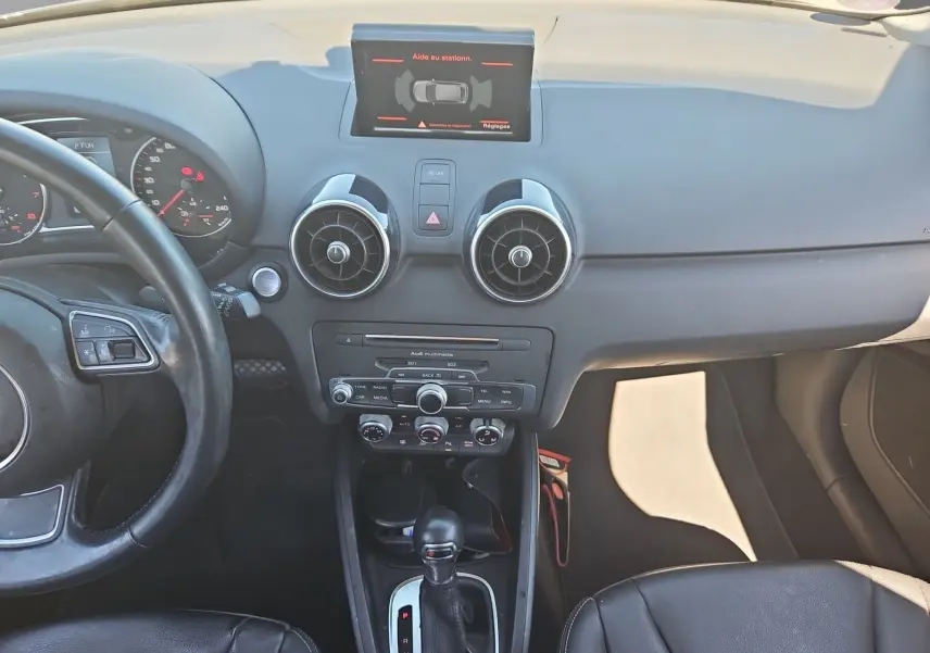 Vue intérieure avant de l’Audi A1 Sportback 2016 noire, mettant en valeur le tableau de bord et la console centrale avec écran tactile.