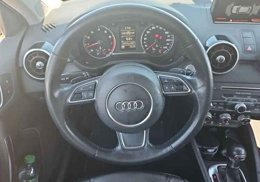 Vue centrée sur le volant sport noir et le tableau de bord de l'Audi A1 Sportback 2016 avec écran tactile et commandes intégrées.