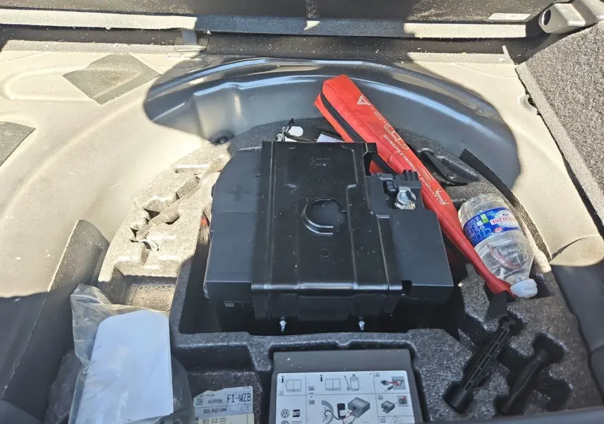 Vue rapprochée du coffre d'une Audi A1 noire, montrant la batterie et le kit anti-crevaison rangés sous le plancher.