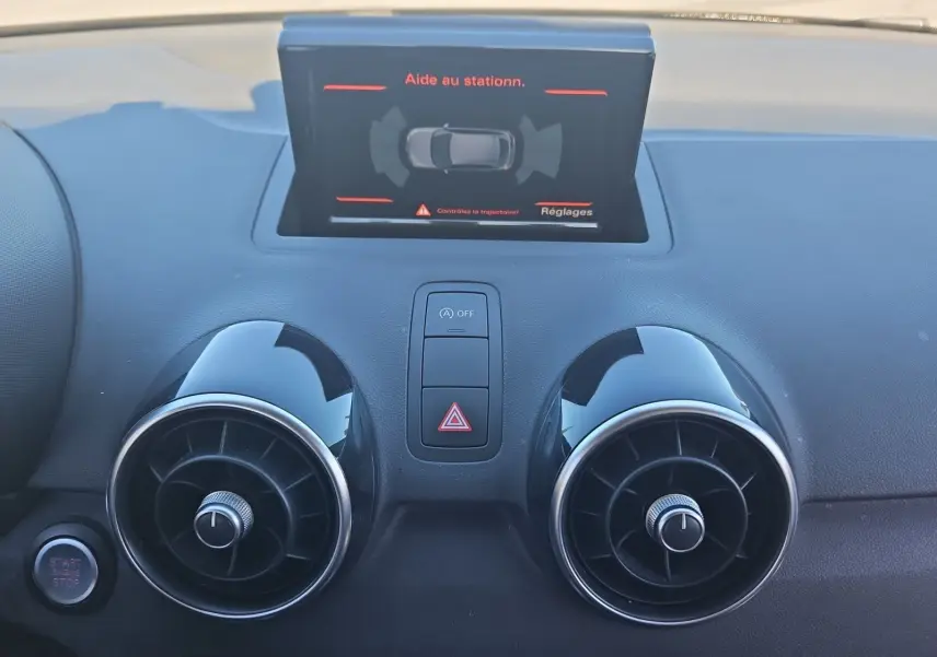 Vue rapprochée du tableau de bord noir de l'Audi A1 Sportback 2016 avec écran d'aide au stationnement et aérateurs ronds.