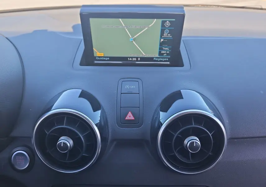 Vue rapprochée du tableau de bord noir d'une Audi A1 Sportback 2016, avec écran GPS et aérateurs ronds chromés.
