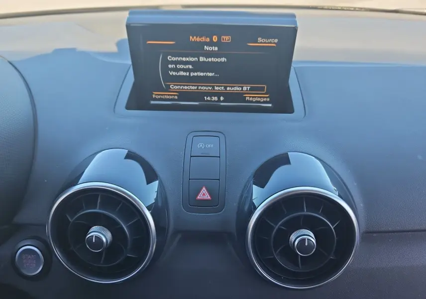 Vue rapprochée du tableau de bord noir de l’Audi A1 avec écran tactile et aérateurs ronds chromés.