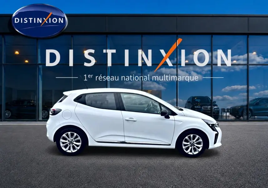 Profil droit d'une Renault Clio V blanche 2025, avec jantes alliage et rétroviseurs noirs, devant une vitrine Distinxion.