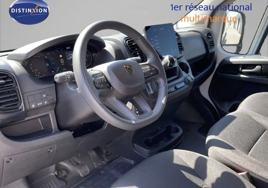 Vue intérieure côté conducteur du Peugeot Boxer Fourgon 2025, montrant le volant, tableau de bord numérique et sièges en tissu noir.