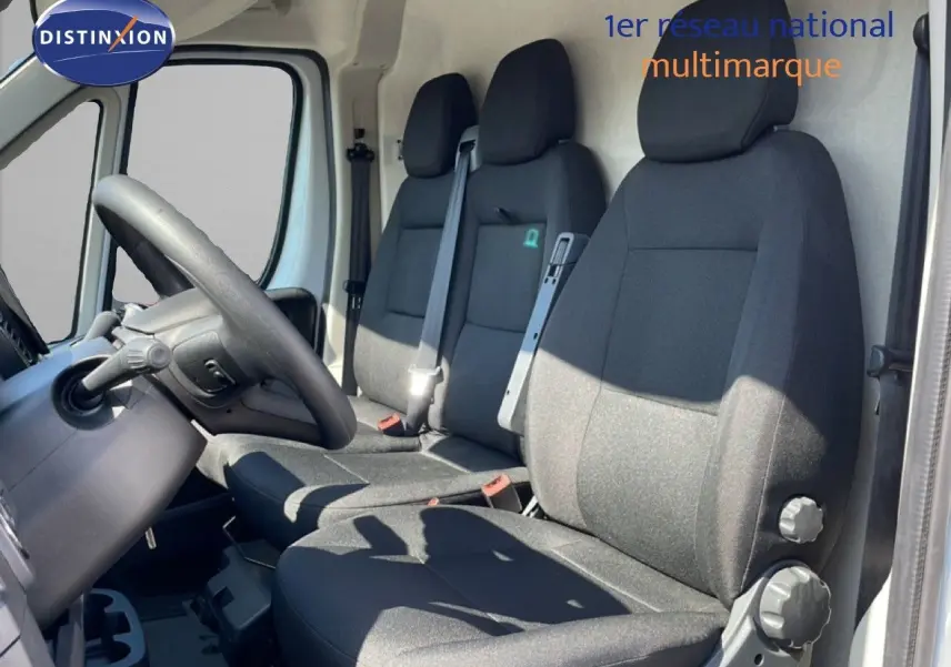 Vue intérieure côté conducteur du Peugeot Boxer Fourgon 2025, sièges tissu noir et volant visible, porte ouverte côté gauche.