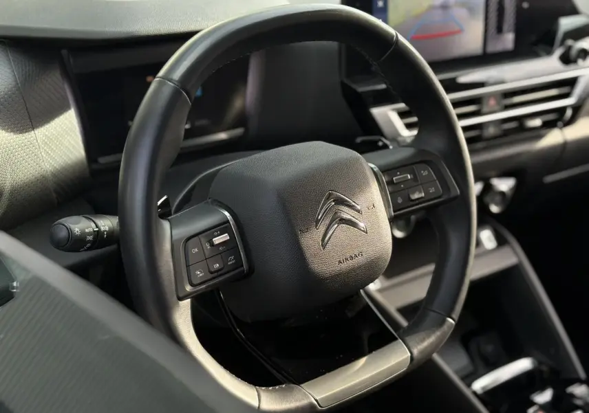 Gros plan sur le volant cuir noir du Citroën C4 X 2024 avec commandes intégrées et tableau de bord moderne en arrière-plan.
