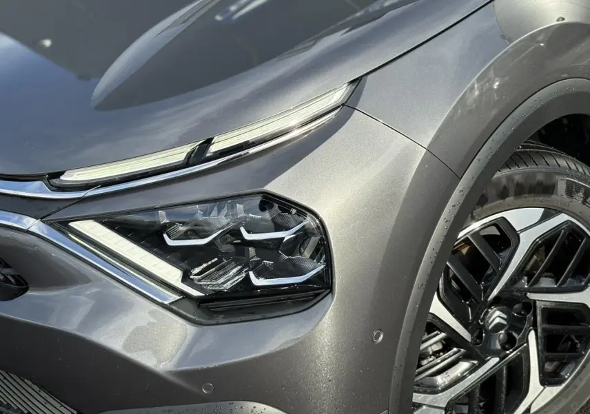 Gros plan sur l'avant droit gris Platinium du Citroën C4 X 2024, mettant en valeur son phare LED et jante alliage diamantée.