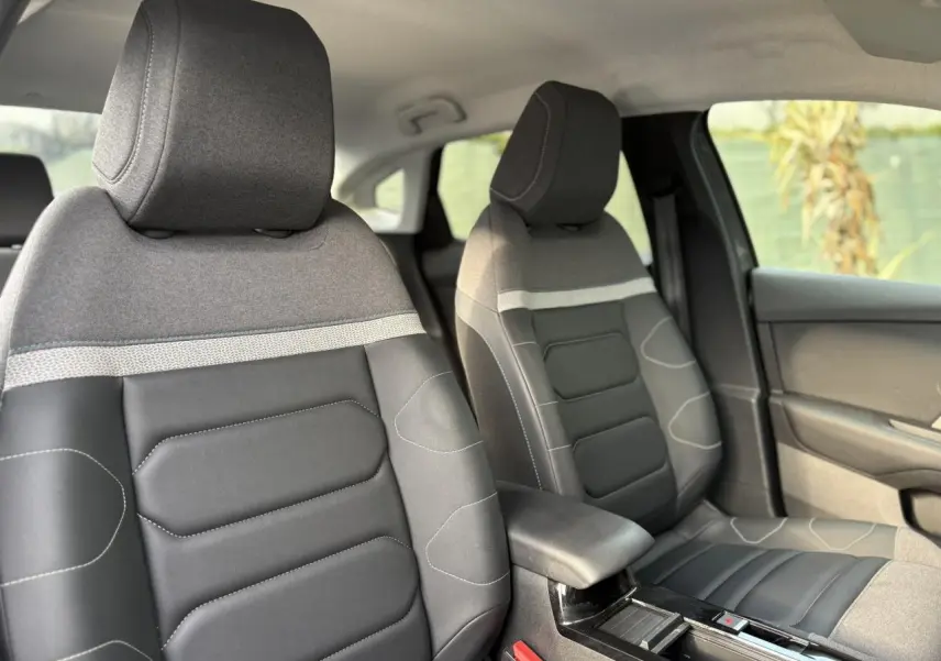 Vue intérieure des sièges avant gris et noirs en tissu et toile enduite du Citroën C4 X 2024, avec accoudoir central.