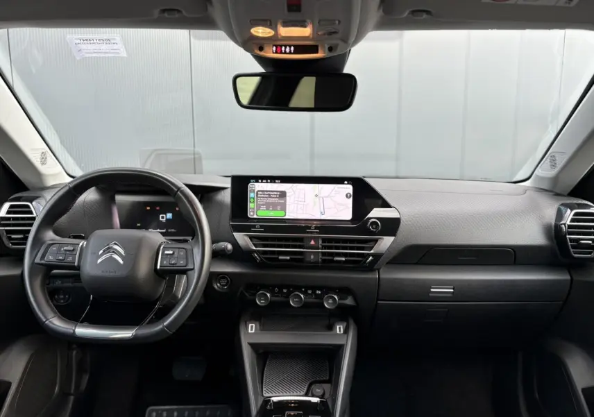 Vue frontale de l’intérieur du Citroën C4 X 2024, tableau de bord noir avec écran tactile et volant cuir.