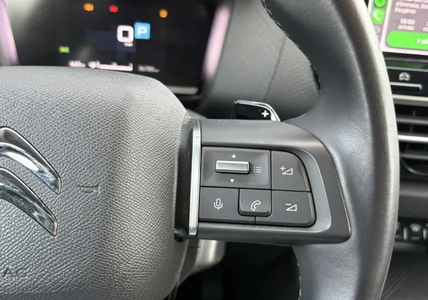 Gros plan sur le côté gauche du volant noir de la Citroën C4 X 2024 avec commandes audio et palettes au volant.